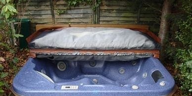 A hot tub in a garden with a cover on it, ready for junk removal.