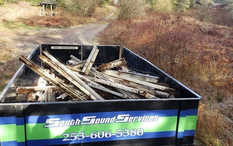 A dump truck full of wood in a wooded area, ready for trash removal in WA.