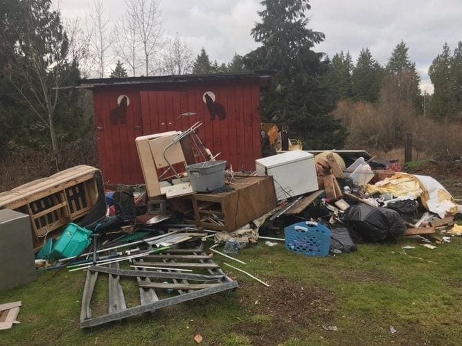 A cluttered mess in front of a red barn, requiring trash removal.